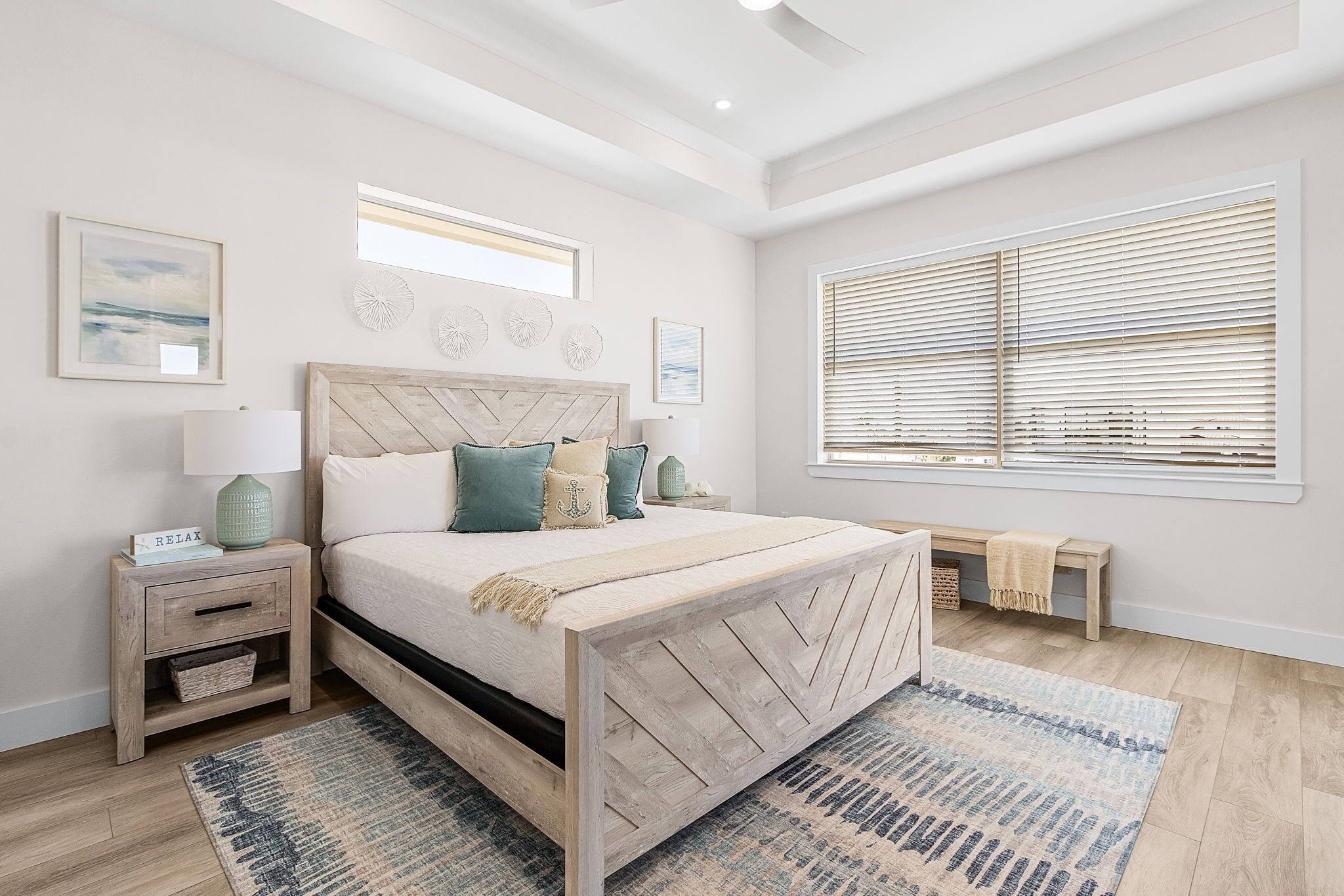 Un dormitorio con cama de madera, mesitas de noche, un banco y un ventanal con persianas.