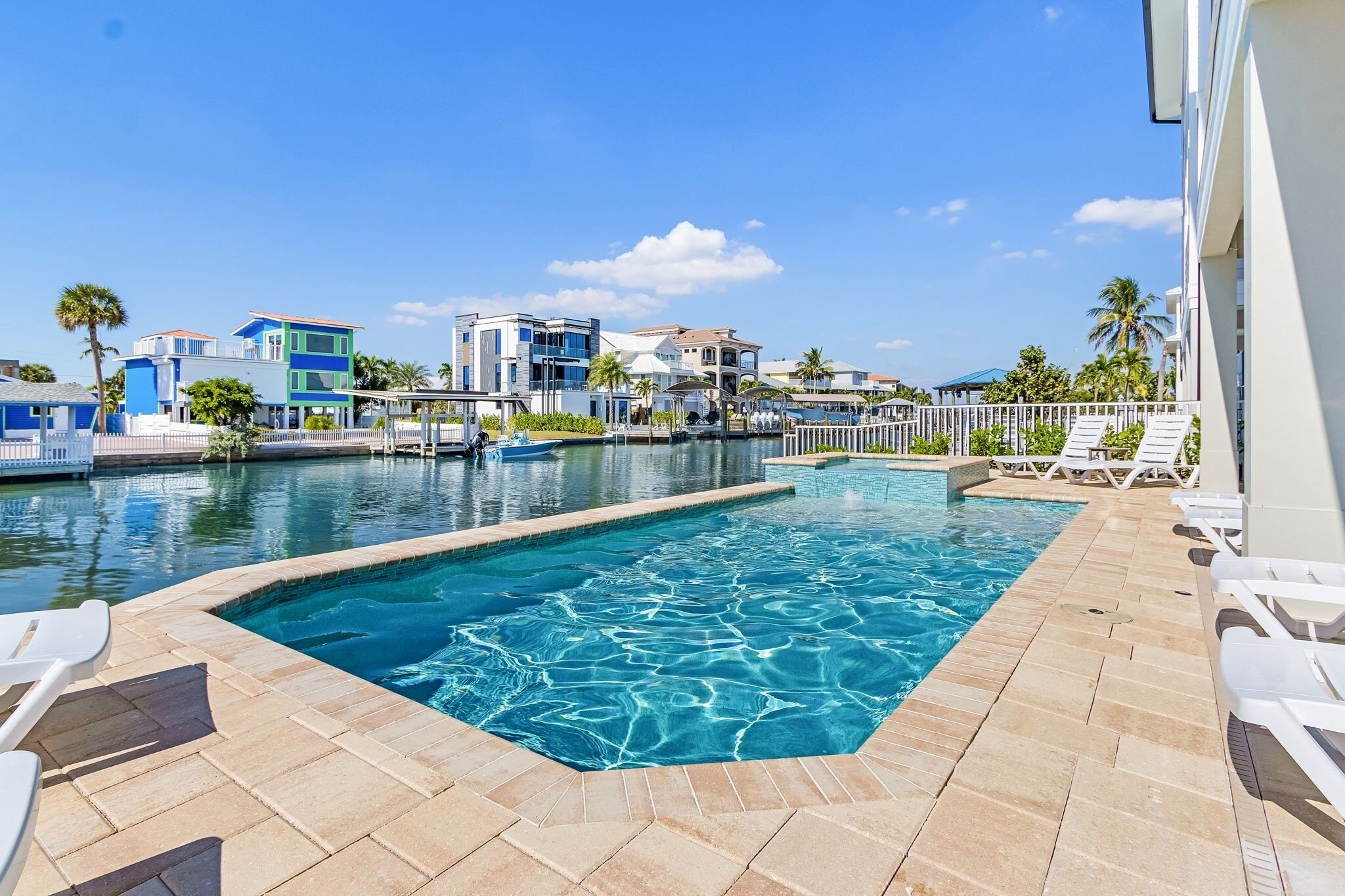 A swimming pool with a tiled deck, lounge chairs, and a view of buildings in the background.