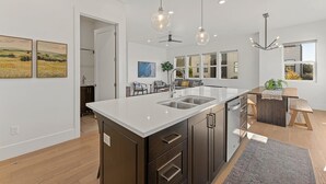 A modern kitchen with a large island, pendant lights, and a view to the dining area.