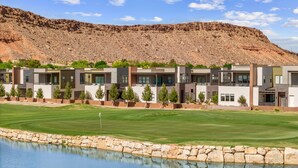 A modern hotel with a pool, a well-maintained lawn, and a mountainous backdrop.