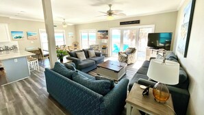 A spacious living room with a large sofa, a coffee table, and a television. There is a balcony with a view of the ocean. - Beachfront Duplex in Morgantown (Gulf Shores)