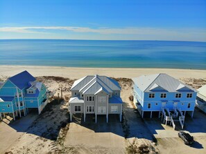 En fastighet vid stranden med tre hus, en sandstrand och havet som bakgrund.