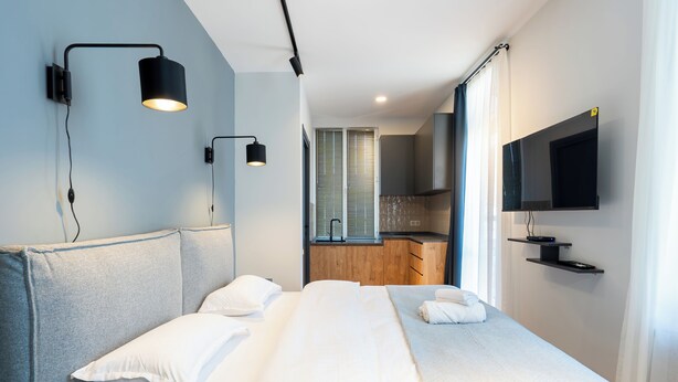 A modern hotel room with a large bed, a TV mounted on the wall, and a kitchenette in the background. - Stones Throw Apartments (Tbilisi)