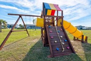 Un parque infantil con tobogán, pared de escalada y columpios.