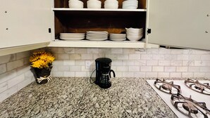 Eine Küche mit weißen Schränken, einer Granit Arbeitsplatte, einer Kaffeemaschine und einem Gasherd.