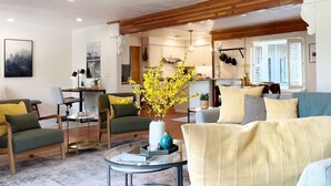 Ein modernes Wohnzimmer mit einem Glastisch, grünen und gelben Sofas und einer Küche im Hintergrund.