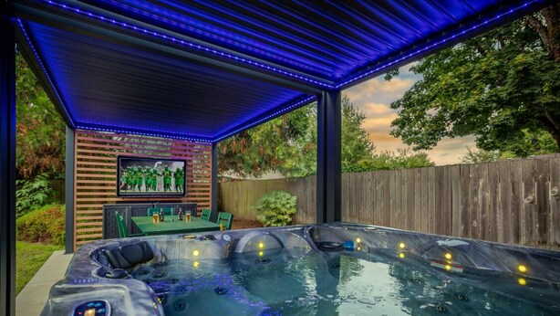 Ein Bereich mit Whirlpool, einer Holzterrasse und einer Pergola mit blauen LED-Leuchten.