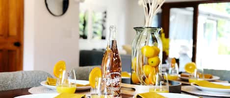 A dining table set with plates, napkins, and a bottle of Bubbly. There is a vase with lemons and decorative balls.