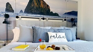 Ein Schlafzimmer mit Bett, Kissen, einem Tablett mit Frühstück und Blick auf den Ozean.