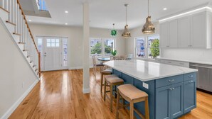 Une cuisine moderne dotée d’un grand îlot central, de planchers en bois et de luminaires suspendus.