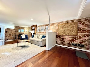 A living room with a brick wall, a sofa, a coffee table, and a fireplace. - Capitol Hill Charm + Walk to Union Station + Free Parking (Washington)