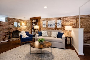 A living room with a brick wall, a fireplace, a sofa, a coffee table, and a bookshelf. - Capitol Hill Charm + Walk to Union Station + Free Parking (Washington)