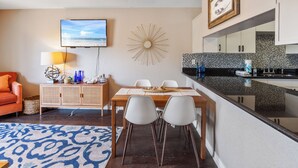 Un salon moderne comprenant un coin repas, un téléviseur fixé au mur et une cuisine dotée d’un plan de travail noir.