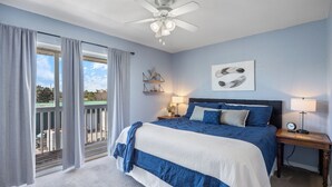 Une chambre à coucher comprenant un lit, deux tables de chevet, un ventilateur de plafond, une fenêtre avec des rideaux et un balcon.