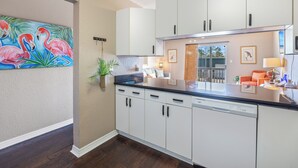 Une cuisine avec des meubles blancs, un plan de travail noir et un tableau représentant des flamants roses accroché au mur.