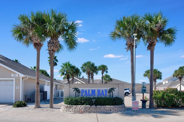Un quartier résidentiel avec une pancarte indiquant « PALM BAY VILLAGE », entouré de palmiers et de maisons.