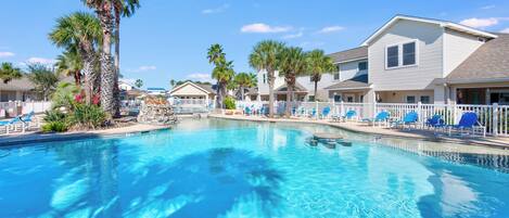 A swimming pool with lounge chairs and palm trees, surrounded by houses.