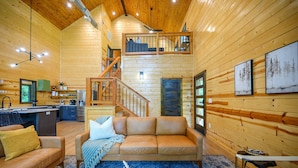 A cozy cabin interior with a wooden interior, a sofa, a coffee table, and a staircase leading to an upper level. - Stylish Cabin Near Broken Bow Lake & Casino + Firewood Provided (Broken Bow)