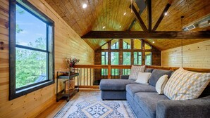 A cozy cabin interior with a large window, a gray sofa, and a patterned rug. - Stylish Cabin Near Broken Bow Lake & Casino + Firewood Provided (Broken Bow)