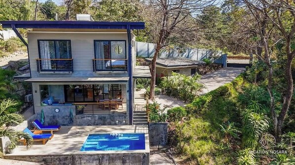Une maison à deux étages avec une piscine, un espace salon extérieur et un jardin.