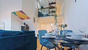 Una sala de estar moderna con un sofá azul, una mesa de comedor de vidrio y sillas, y una escalera que conduce a un nivel superior.