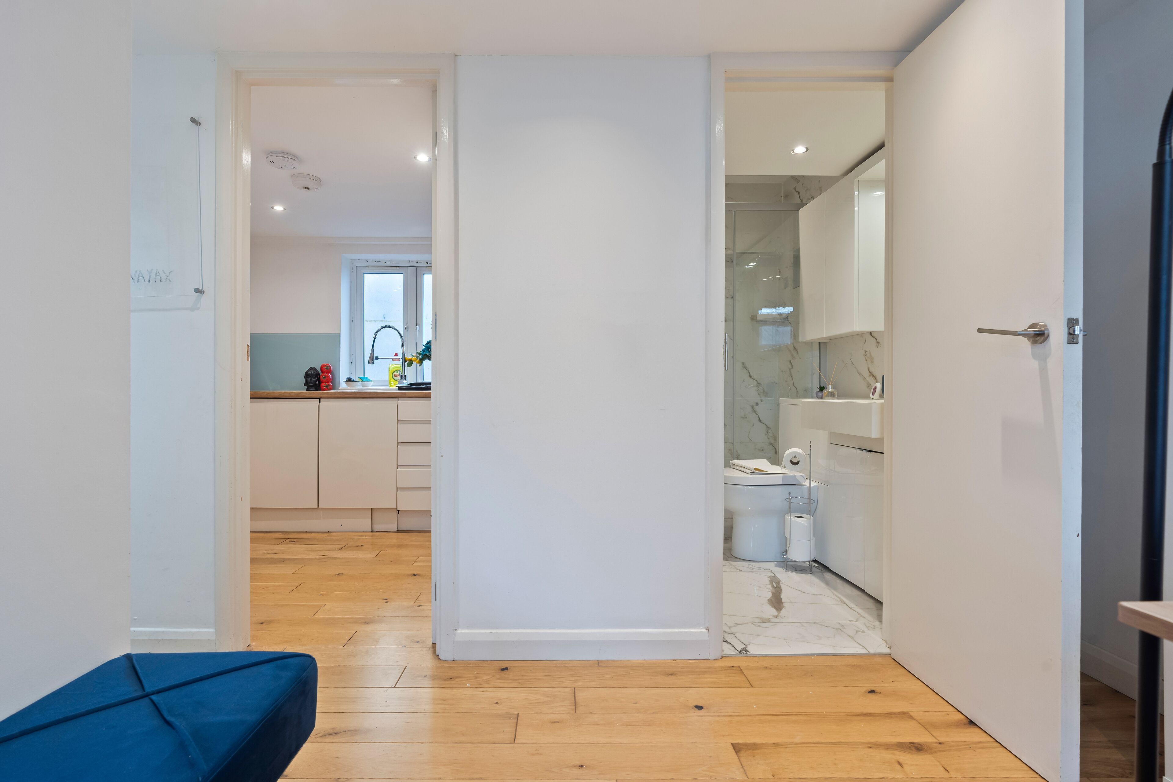 Una cocina moderna con armarios blancos, piso de madera y vista al baño contiguo.