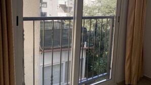 A room with a sliding glass door leading to a balcony. The balcony has a metal railing and a view of neighboring buildings and greenery. - Comfort Room -A- (Marmaris)