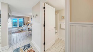 A hallway with a white door, a dining area with a table and chairs, and a view of the outside through a window.