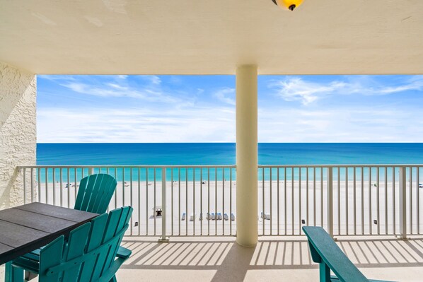 A balcony with a view of the beach, a table, and chairs.