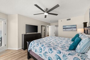 Ein Schlafzimmer mit einem Bett, einem Deckenventilator, einem Fernseher, einer Kommode und einer Tür.
