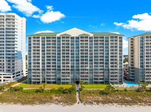 A high-rise hotel with multiple balconies, a swimming pool, and a beach view.