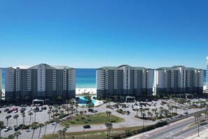 A hotel with a pool, parking lot, and beach view.