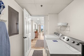 Ein Hotelzimmer mit Bett, Waschmaschine, einem kleinen Tisch mit Pflanze und Meerblick durch ein Fenster.
