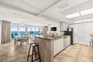 A spacious kitchen with a large island, a dining area with a view, and a modern ceiling design. - FREE Beach Service for 4! Long Beach 4-701, Walk in Showers, Pools & Hot Tubs (Panama City Beach)