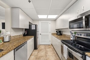 A modern kitchen with granite countertops, stainless steel appliances, and white cabinetry.