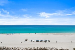 A beach with a row of beach chairs, a lifeguard tower, and a sandy foreground. - FREE Beach Service for 4! Long Beach 4-701, Walk in Showers, Pools & Hot Tubs (Panama City Beach)