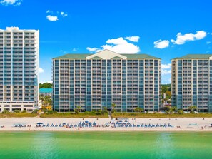 A beachfront hotel with multiple high-rise buildings, a sandy beach, and clear blue skies.