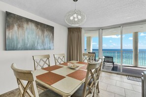 A dining area with a checkered table, chairs, and a view of the ocean through large glass doors.