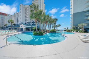 A hotel pool area with multiple pools, palm trees, and lounge chairs.