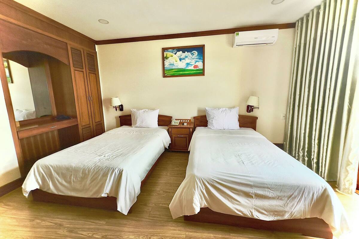 Une chambre d’hôtel avec deux lits, des têtes de lit en bois, un tableau au mur et un appareil de climatisation.
