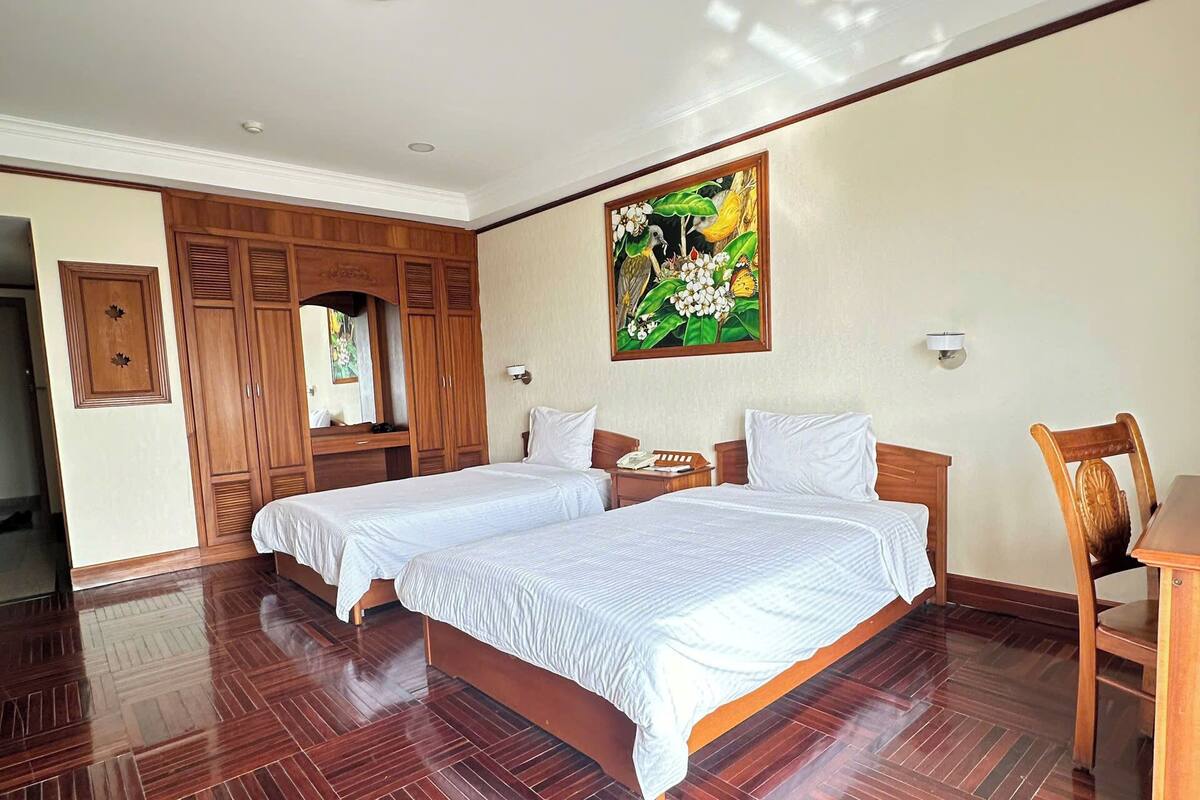 Une chambre spacieuse avec deux lits, un plancher en bois et un grand tableau accroché au mur.