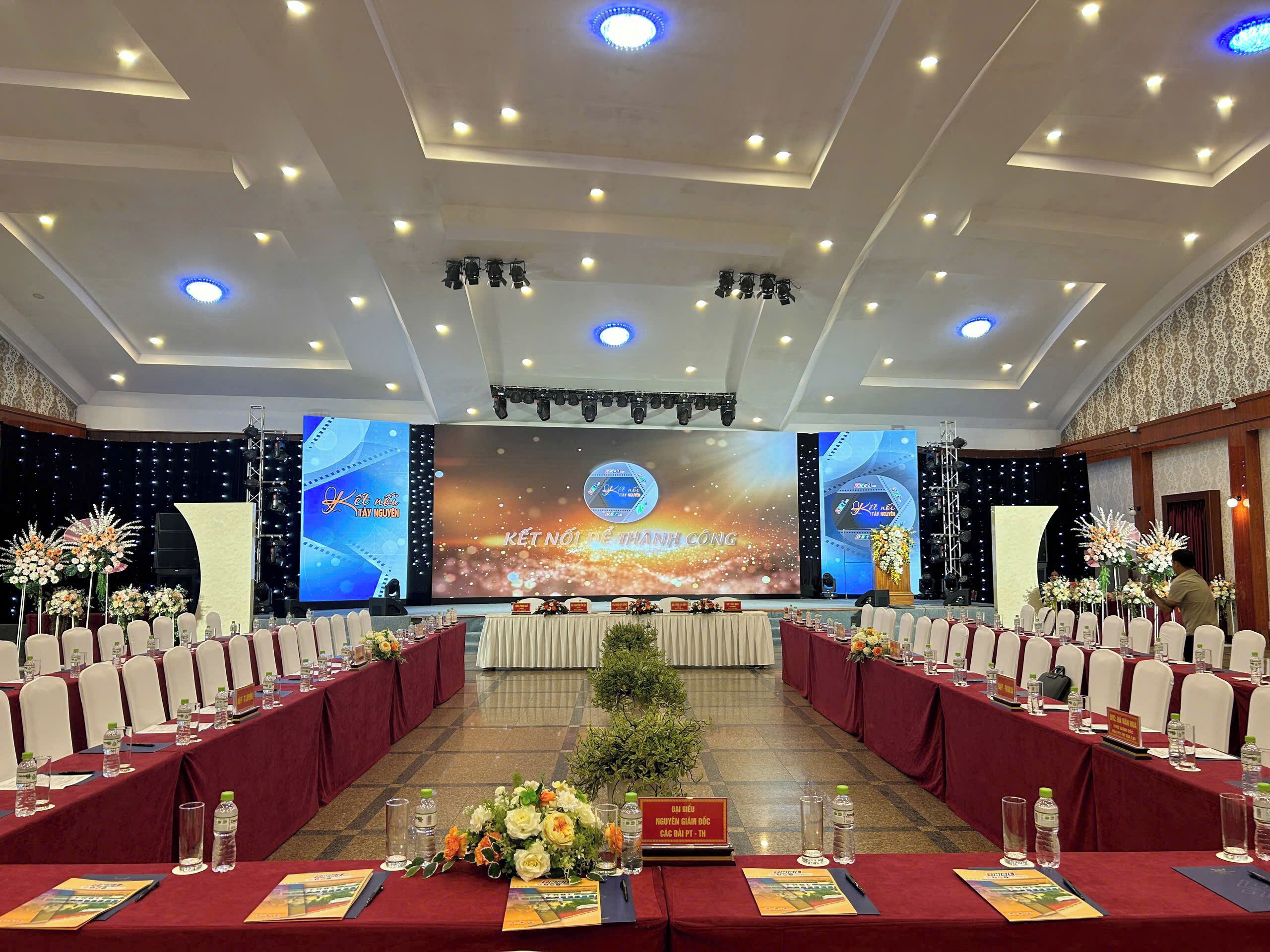 Une salle de conférence dotée d’une scène, de plusieurs tables avec des plaques nominatives et agrémentée de compositions florales.