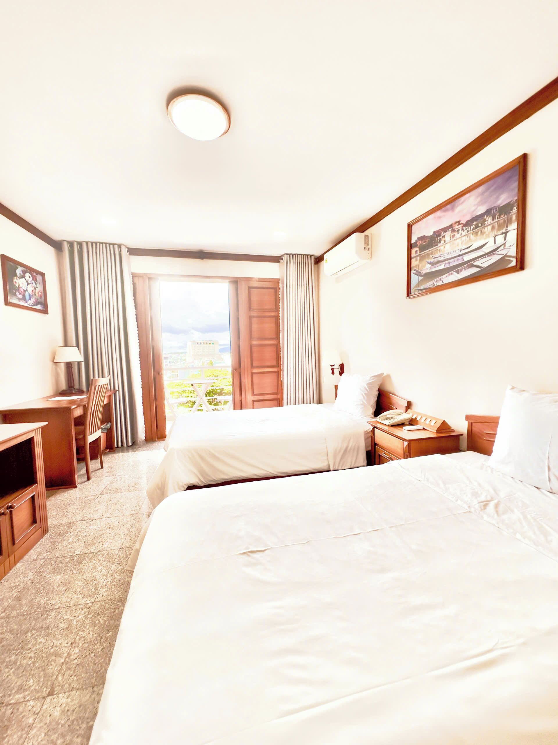 A hotel room with two beds, a desk, a chair, a lamp, and a painting.