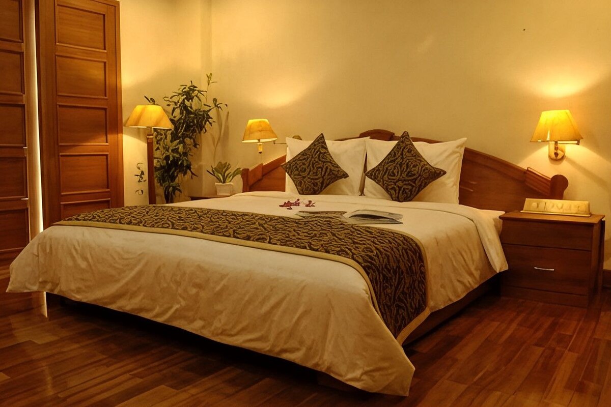 Une chambre d’hôtel avec un grand lit, deux tables de chevet avec des lampes, une armoire en bois et une plante en pot.
