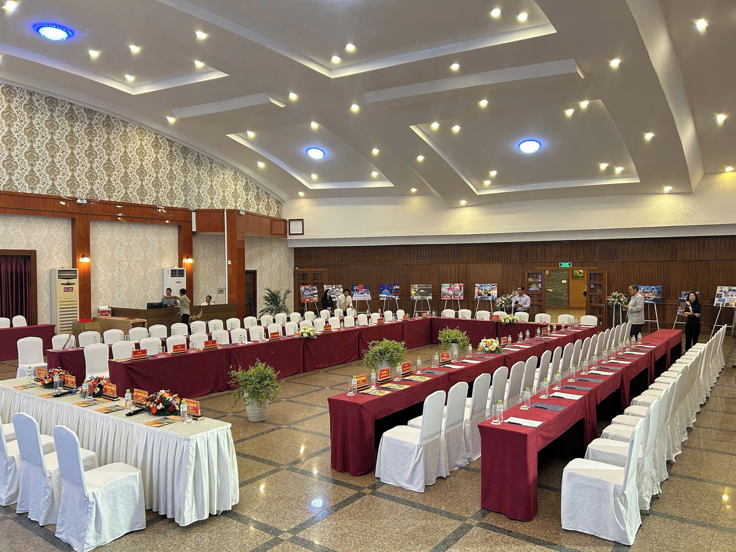 A large conference room with rows of tables and chairs, a stage with a podium, and a patterned wall.