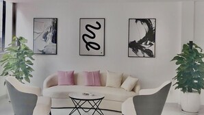 A modern living room with a white sofa, two armchairs, a coffee table, and three framed artworks on the wall. - Muong Thanh Grand Gia Lai (Pleiku)