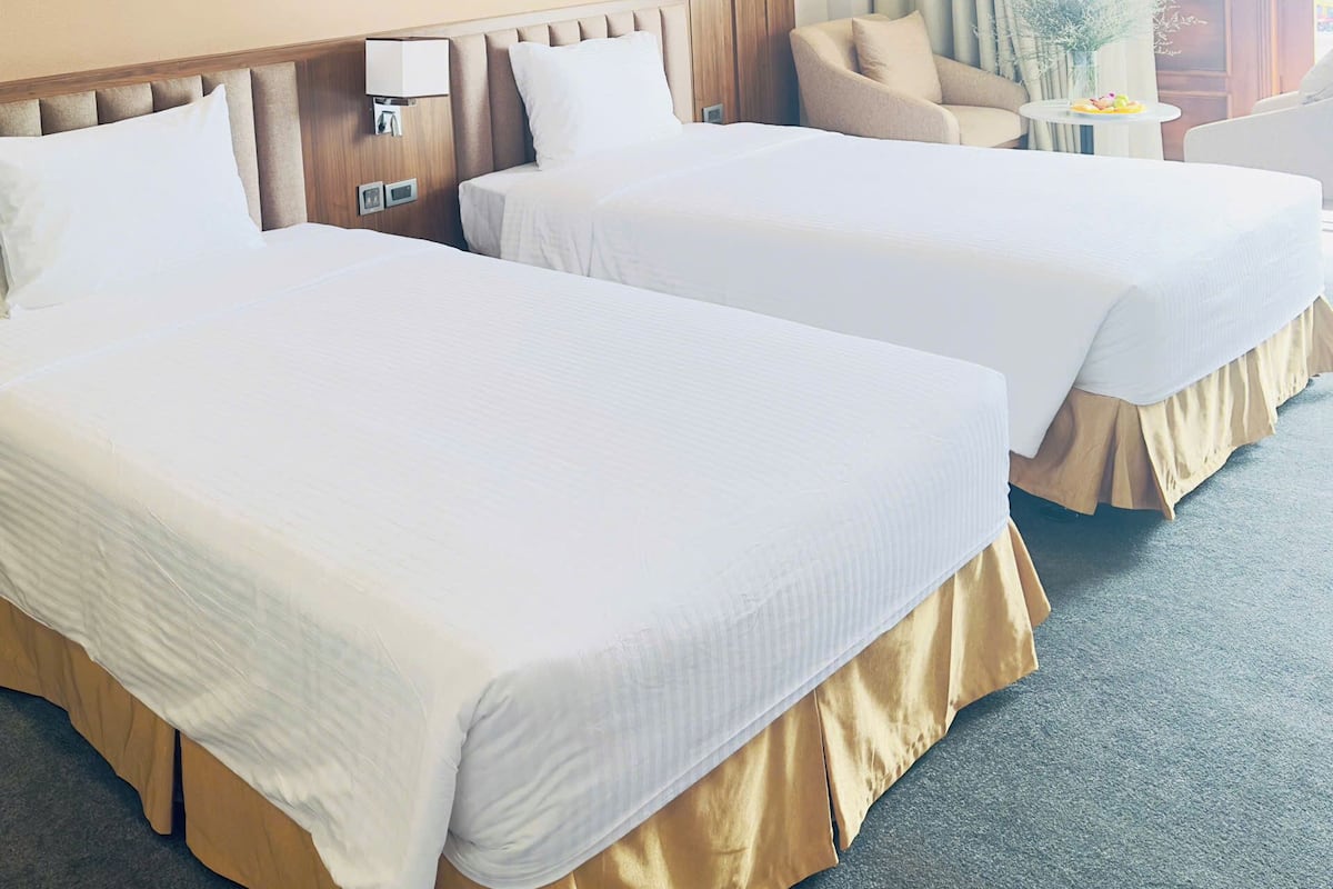Une chambre d’hôtel avec deux lits, un canapé, une petite table et une fenêtre avec des rideaux.