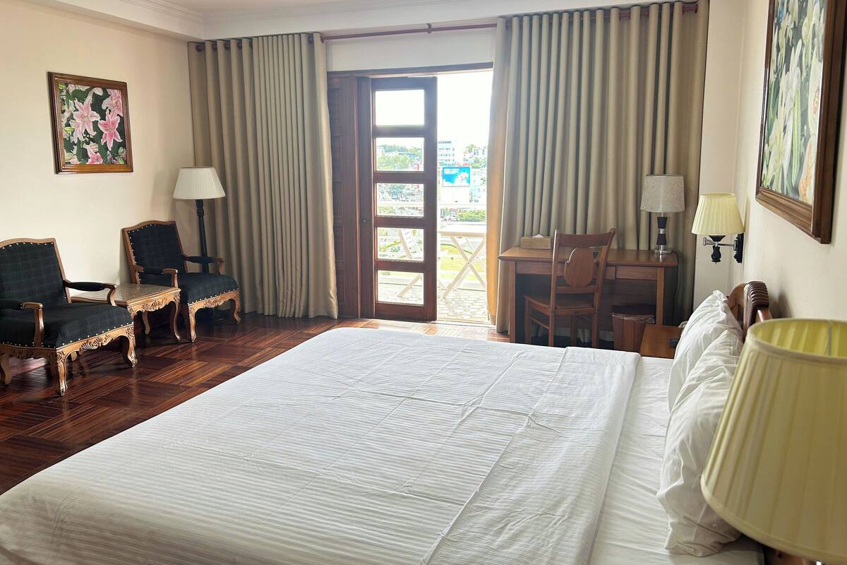 Une chambre d’hôtel avec un grand lit, deux fauteuils, un bureau et une vue sur l’extérieur.