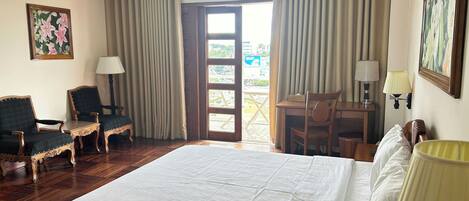 A hotel room with a large bed, two chairs, a desk, and a view of the outdoors.