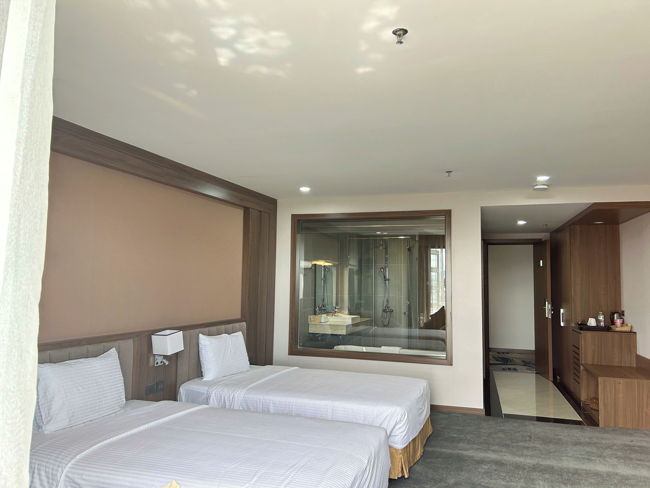 A hotel room with two beds, a large mirror, a shower area, and a wardrobe.